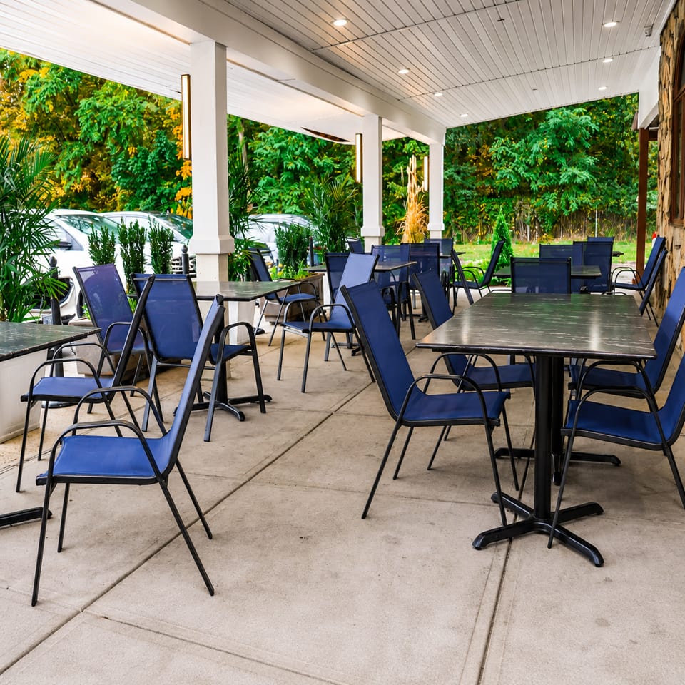 Outdoor patio dining area with blue chairs and dark tables under a white covered porch.